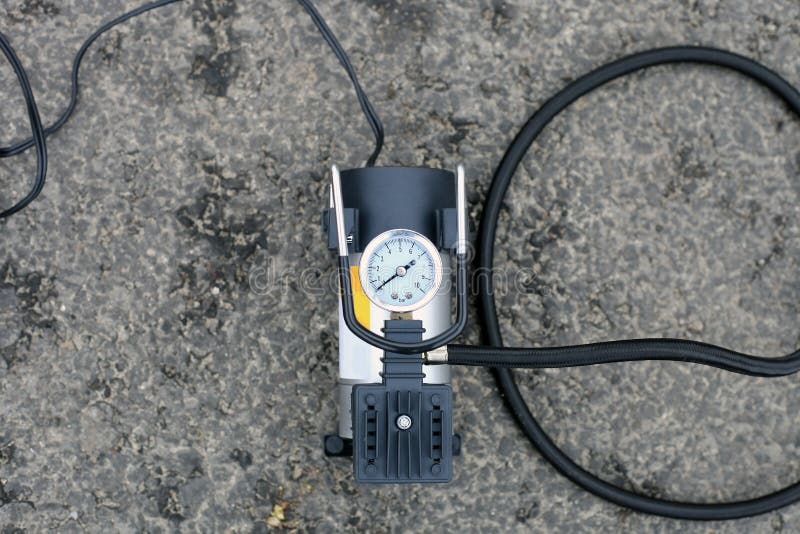 Tire inflator car tool on road. Portable metal air compressor pump for car wheels, driver equipment