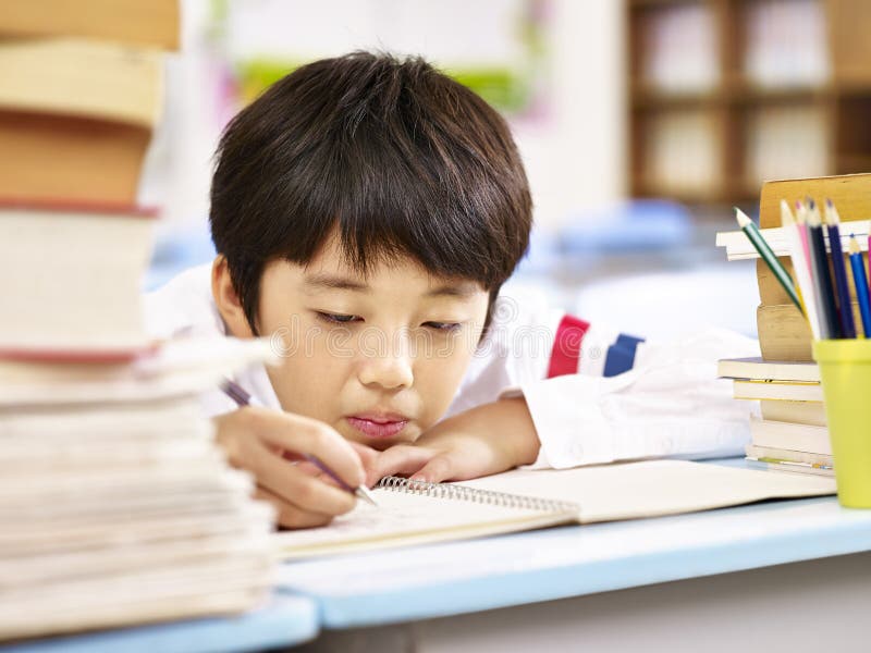Tired and bored asian schoolboy doing homework in classroom royalty free stock photo