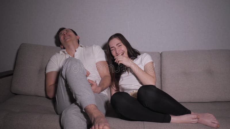 Tired and bored couple sitting lazily on a sofa at night watching tv