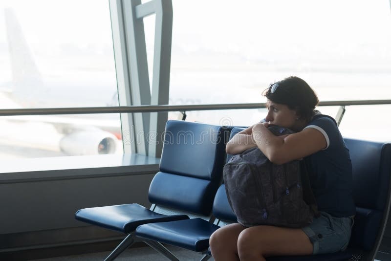 Tired caucasian woman in airport hall. Girl waiting her flight at airport terminal, holding her bag in hands. stock photo Tired caucasian woman in airport hall. Girl waiting her flight at airport terminal, holding her bag in hands. stock photo