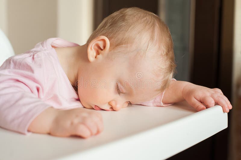 Tired child sleeping in highchair after the lunch. Cute baby girllying his face on the table tray.