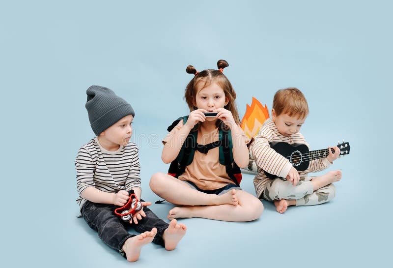 Tired children sitting next to fake campfire, playing their instruments