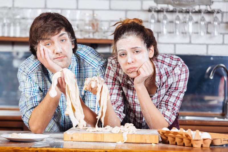 Tired exhausted young couple with flour on their faces kneading dough on the kitchen. Tired exhausted young couple with flour on their faces kneading dough on the kitchen