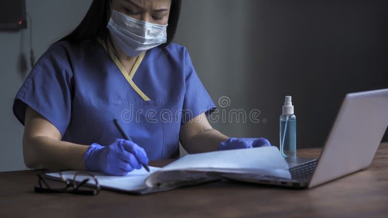 Tired female doctor fills out medical forms, Woman writes with a pen on paper sitting at desk while working on computer