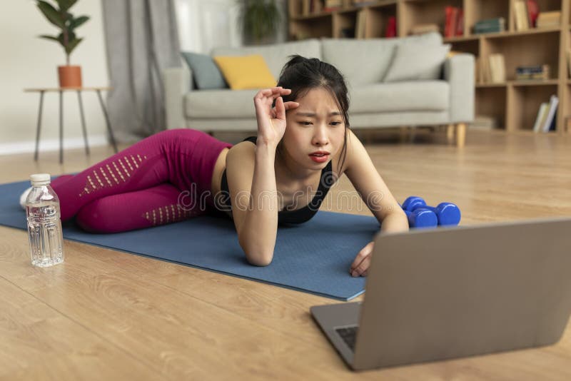 Tired Fit Chinese Lady Lying on Yoga Mat in Front of Laptop and Wiping ...