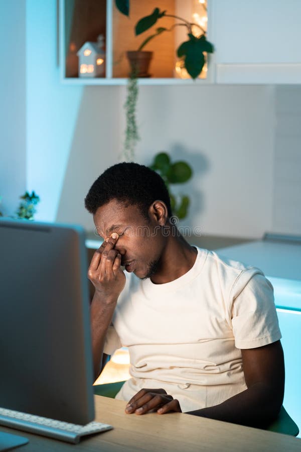 Tired freelance programmer man massage nose suffer from eyestrain working remote at computer at home stock photography
