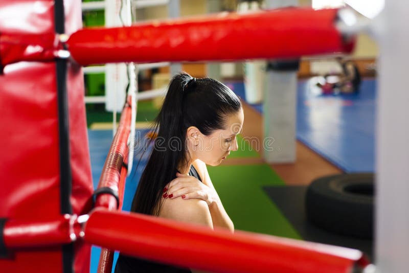 Tired girl athlete sitting in the boxing ring. beautiful woman holding herself by the shoulder.