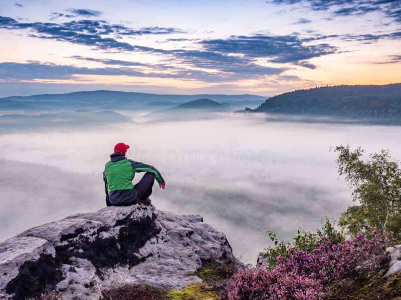 Tired hiker sits on the edge of the cliff and looking at the sun valley. Adventure un misty mountains. Tired hiker sits on the edge of the cliff and looking at the sun valley. Adventure un misty mountains