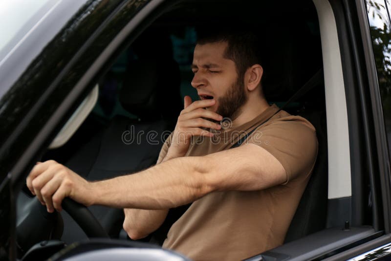 Tired man yawning while driving his car