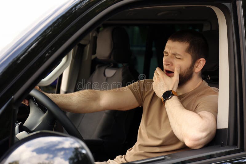 Tired man yawning while driving his modern car