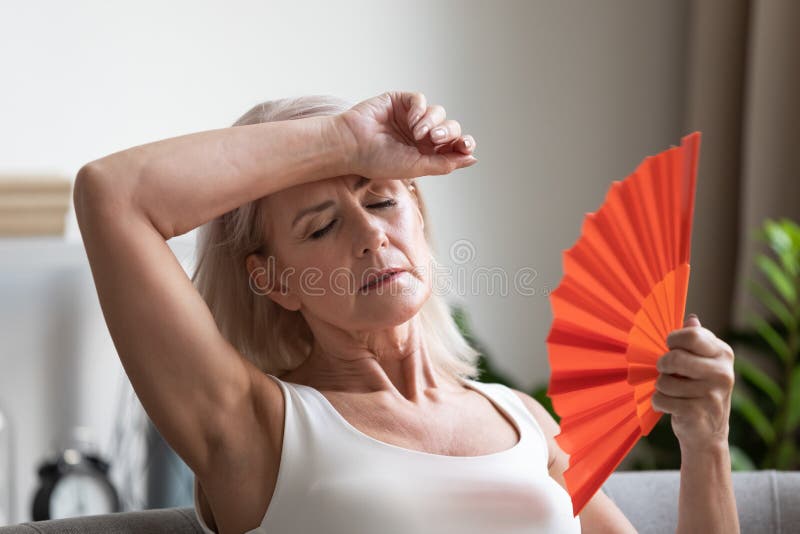 Tired overheated middle aged lady wave fan suffer from menopause exhaustion complain on heat at home, stressed old woman sweat feel uncomfortable hot in summer weather problem without air conditioner. Tired overheated middle aged lady wave fan suffer from menopause exhaustion complain on heat at home, stressed old woman sweat feel uncomfortable hot in summer weather problem without air conditioner