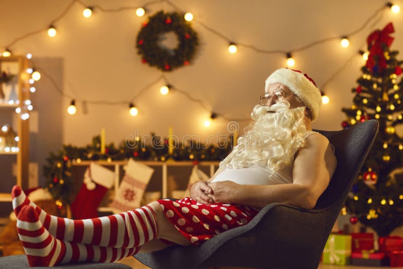 Tired Santa relaxing in comfy armchair after long workday and watching Christmas TV show