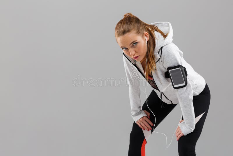 Tired sports woman runner standing isolated listening music by earphones.