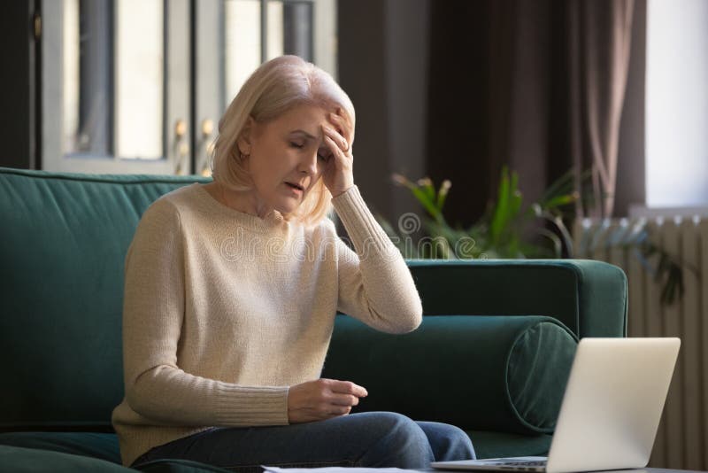 Tired stressed upset middle aged mature woman feeling sick headache after computer work sit at home on sofa, sad fatigued old senior lady grandmother touching head suffering from ache pain migraine. Tired stressed upset middle aged mature woman feeling sick headache after computer work sit at home on sofa, sad fatigued old senior lady grandmother touching head suffering from ache pain migraine