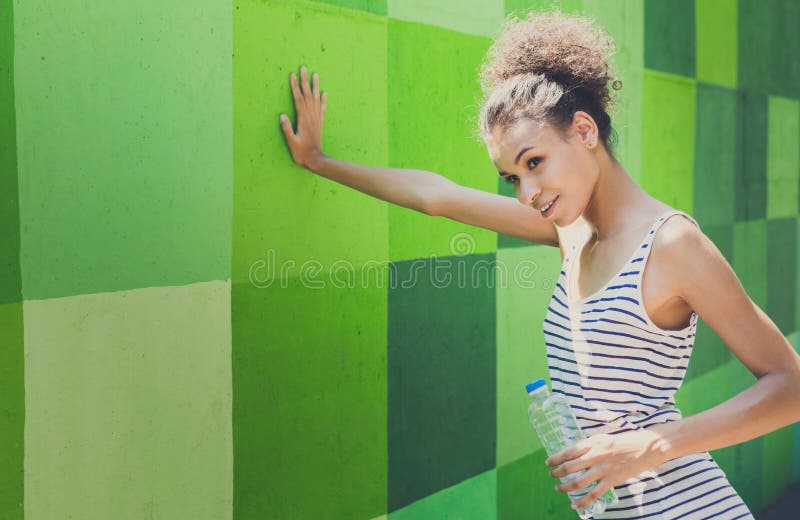 Tired woman runner is having break, leaning on green wall