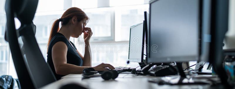 Tired woman workaholic t-shirt works in an empty office and holds fingers on the bridge of the nose. A girl with a