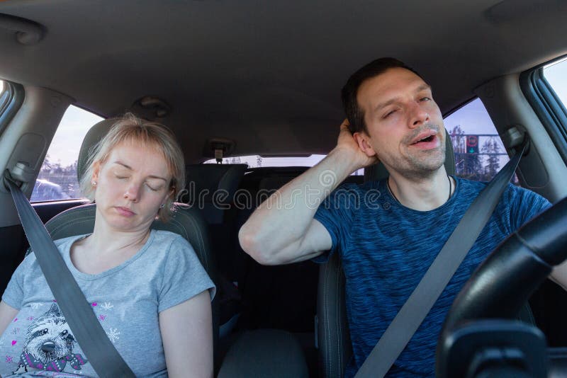 Tired yawning man driving a car and sleeping woman together during road trip. Passengers and driver wearing seat safety belts