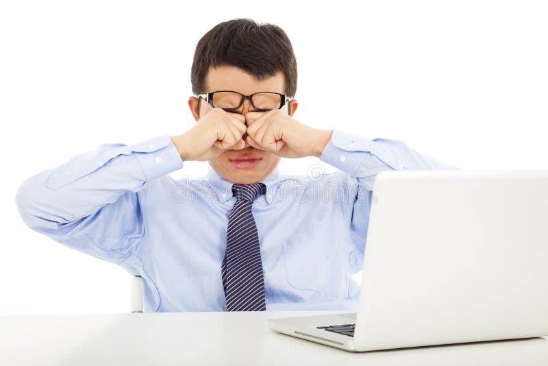 Tired young businessman rubbing his eyes with laptop in office