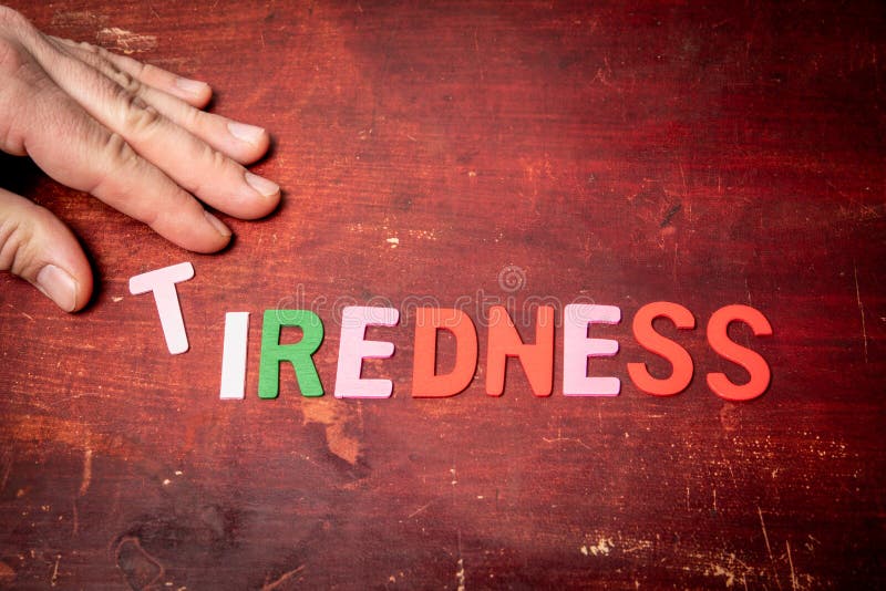 TIREDNESS Concept. Text from colorful letters on wood texture background stock image