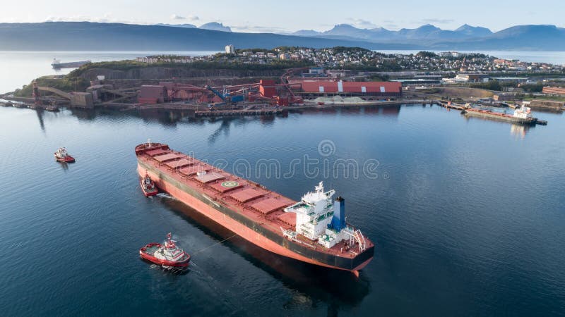 Tiro aéreo de um terminal de aproximação do porto do navio de carga com ajuda do navio do reboque fotos de stock royalty free Tiro aéreo de um terminal de aproximação do porto do navio de carga com ajuda do navio do reboque fotos de stock royalty free