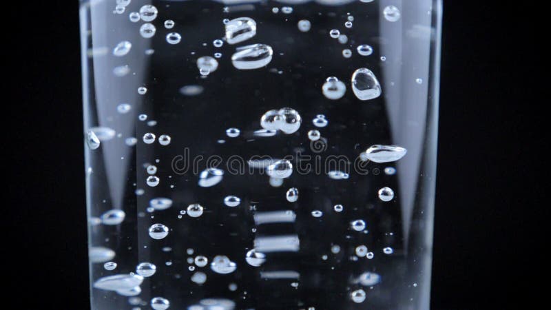 Tiro cercano del vidrio de colada de agua, muchas burbujas en el líquido, fondo negro, vídeo de alta calidad almacen de metraje de vídeo