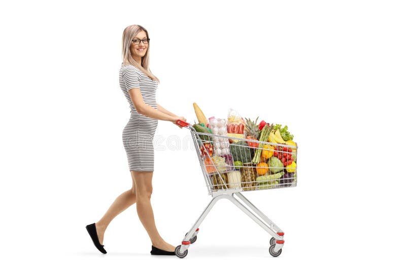 Tiro completo do comprimento de uma mulher atrativa nova que empurra um carrinho de compras com produtos alimentares e que sorri imagem de stock royalty free Tiro completo do comprimento de uma mulher atrativa nova que empurra um carrinho de compras com produtos alimentares e que sorri imagem de stock royalty free
