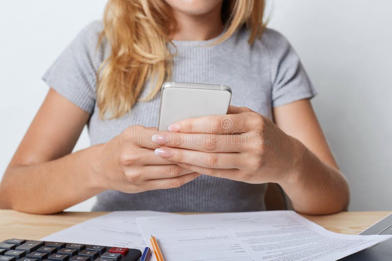 Tiro cosechado del enterpreneur femenino joven en camiseta gris, sosteniendo el teléfono elegante en las manos, descansando para imagenes de archivo Tiro cosechado del enterpreneur femenino joven en camiseta gris, sosteniendo el teléfono elegante en las manos, descansando para imagenes de archivo