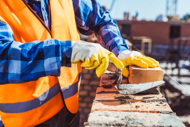 Tiro cosechado del trabajador de construcción en los guantes protectores que ponen ladrillos foto de archivo libre de regalías