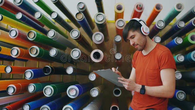 Tiro da zorra do trabalhador novo feliz no armazém industrial que escuta a música e que dança durante o trabalho Homem nos auscul fotografia de stock royalty free Tiro da zorra do trabalhador novo feliz no armazém industrial que escuta a música e que dança durante o trabalho Homem nos auscul fotografia de stock royalty free
