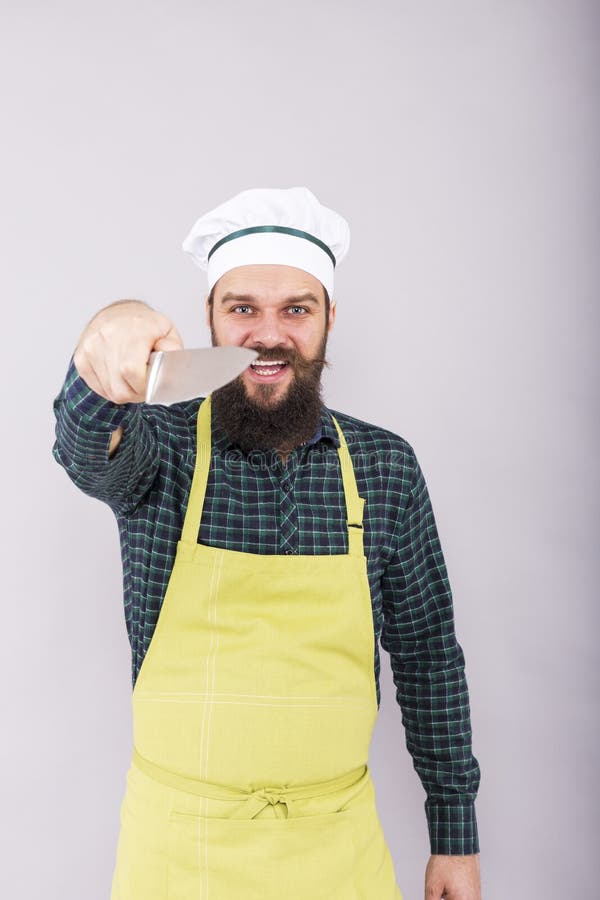 Tiro del estudio de un hombre joven barbudo con holdi del sombrero del delantal y del cocinero fotografía de archivo libre de regalías Tiro del estudio de un hombre joven barbudo con holdi del sombrero del delantal y del cocinero fotografía de archivo libre de regalías