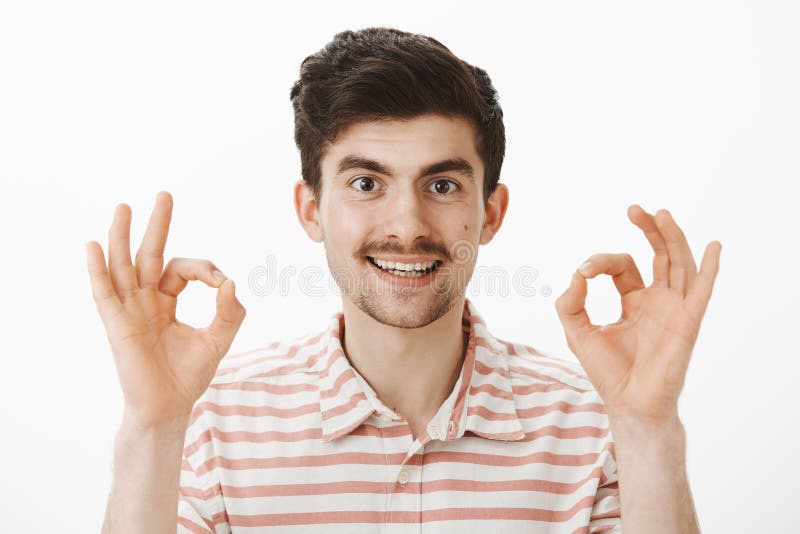 Tiro del estudio del hombre atractivo interesado satisfecho con el bigote, aumentando los fingeres y mostrando muy bien o gesto a fotografía de archivo Tiro del estudio del hombre atractivo interesado satisfecho con el bigote, aumentando los fingeres y mostrando muy bien o gesto a fotografía de archivo