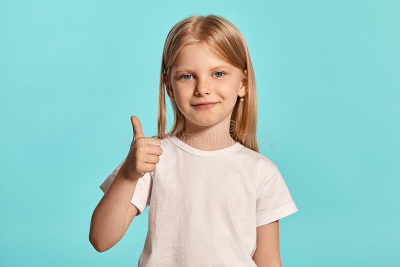 Tiro del estudio del primer de una niña rubia preciosa en una camiseta blanca que presenta contra un fondo azul fotografía de archivo libre de regalías Tiro del estudio del primer de una niña rubia preciosa en una camiseta blanca que presenta contra un fondo azul fotografía de archivo libre de regalías