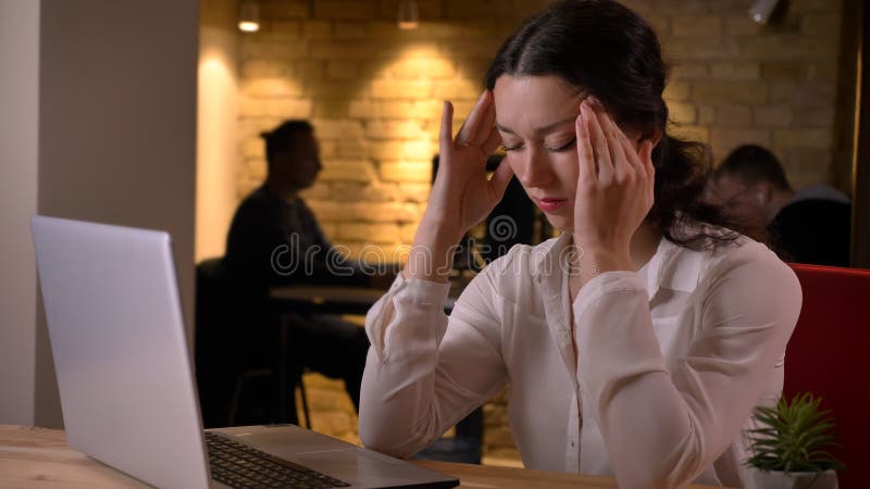 Tiro del primo piano di giovane donna di affari caucasica graziosa che ha un'emicrania mentre scrivendo sul computer portatile al immagini stock libere da diritti Tiro del primo piano di giovane donna di affari caucasica graziosa che ha un'emicrania mentre scrivendo sul computer portatile al immagini stock libere da diritti