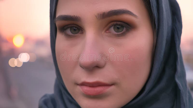 Tiro del primo piano di giovane fronte femminile attraente nel hijab che esamina diritto la macchina fotografica con la città urb immagine stock libera da diritti Tiro del primo piano di giovane fronte femminile attraente nel hijab che esamina diritto la macchina fotografica con la città urb immagine stock libera da diritti