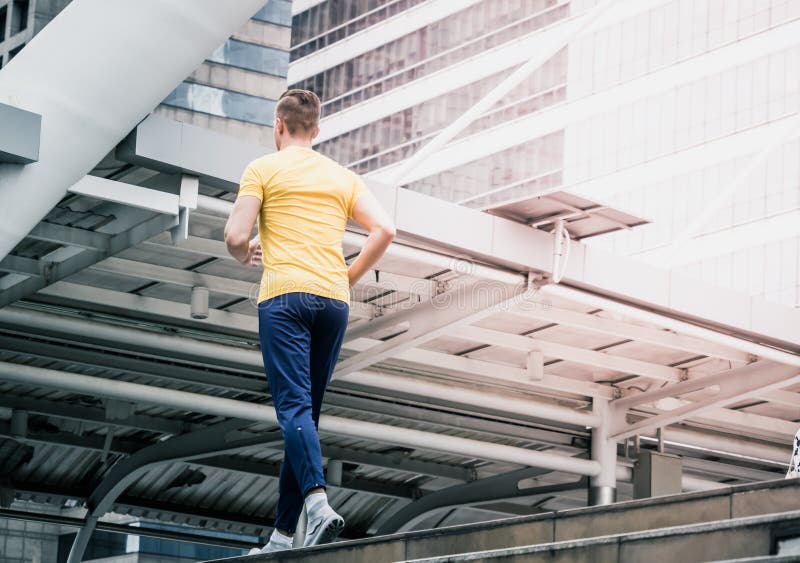 Tiro do homem no amarelo que movimenta-se para fora na cidade moderna corredor masculino que dá certo na cidade moderna foto de stock Tiro do homem no amarelo que movimenta-se para fora na cidade moderna corredor masculino que dá certo na cidade moderna foto de stock
