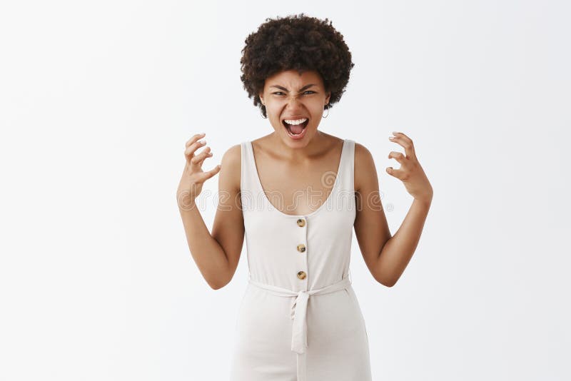 Tiro horizontal de la mujer asustadiza ultrajada en los guardapolvos blancos con el peinado afro que gesticula las manos con enoj fotografía de archivo Tiro horizontal de la mujer asustadiza ultrajada en los guardapolvos blancos con el peinado afro que gesticula las manos con enoj fotografía de archivo