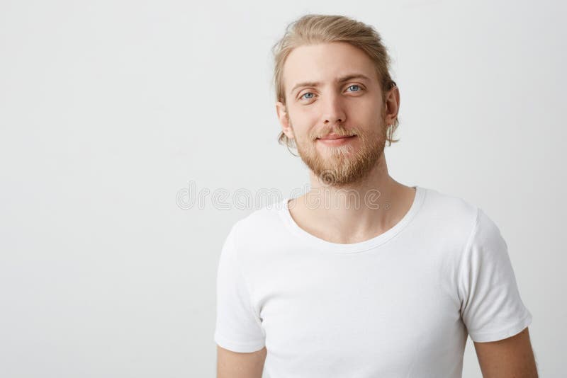 Tiro interno do homem louro caucasiano bonito positivo com barba e do bigode que smirking ao olhar a câmera e imagens de stock royalty free Tiro interno do homem louro caucasiano bonito positivo com barba e do bigode que smirking ao olhar a câmera e imagens de stock royalty free
