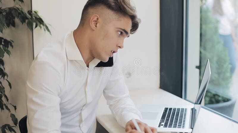 Tiro medio del hombre de negocios joven concentrado que toma notas en cuaderno al hablar en el teléfono durante descanso para tom