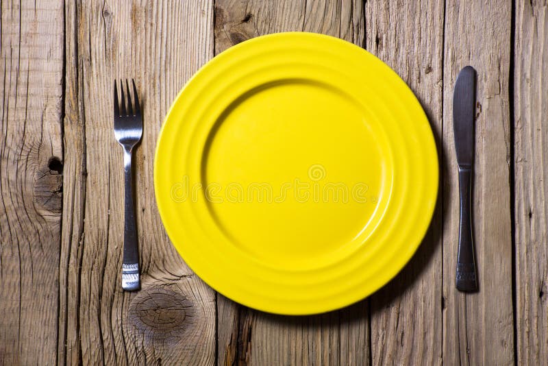 Tischbesteck und gelbe Platte auf hölzernem