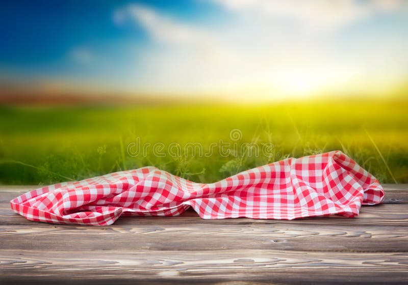 Red picnic table cloth on wooden table empty space nature sunset field background.Food advertisment template. Red picnic table cloth on wooden table empty space nature sunset field background.Food advertisment template.