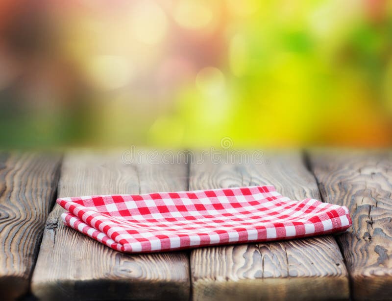 Red picnic table cloth napkin on wooden plank table blur nature background.Retro design empty space food advertisement icon. Red picnic table cloth napkin on wooden plank table blur nature background.Retro design empty space food advertisement icon