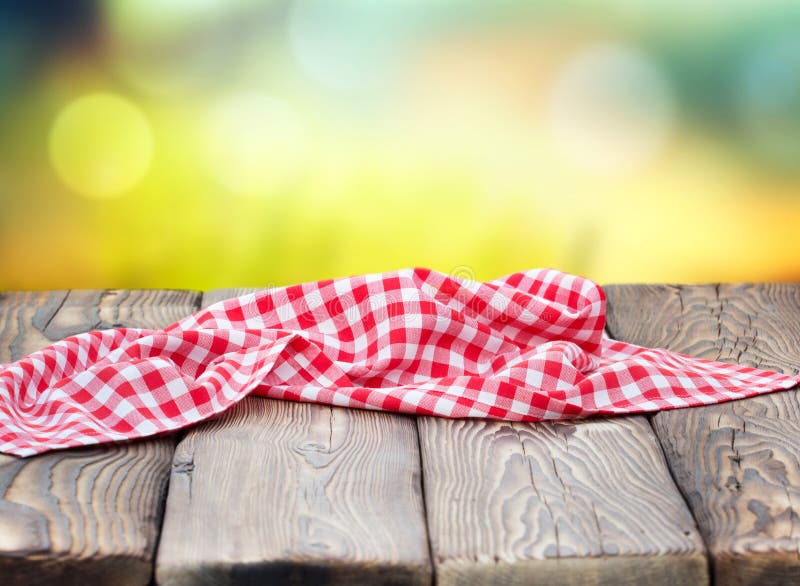 Red picnic table cloth napkin on wooden plank table blur nature background.Empty space table food design advertisement template. Red picnic table cloth napkin on wooden plank table blur nature background.Empty space table food design advertisement template.