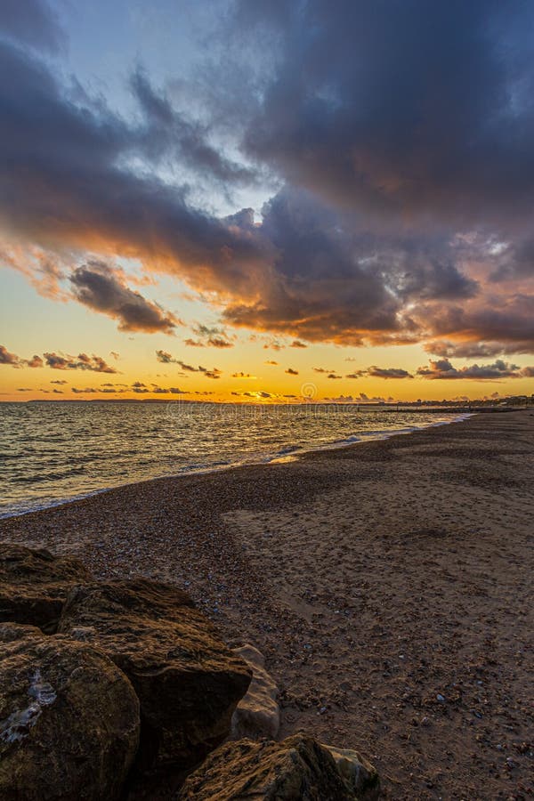 Titel: En bild av en stonstrand vid solnedgången med krasande vågor och eko under en stor gul grumlig himmel royaltyfri bild