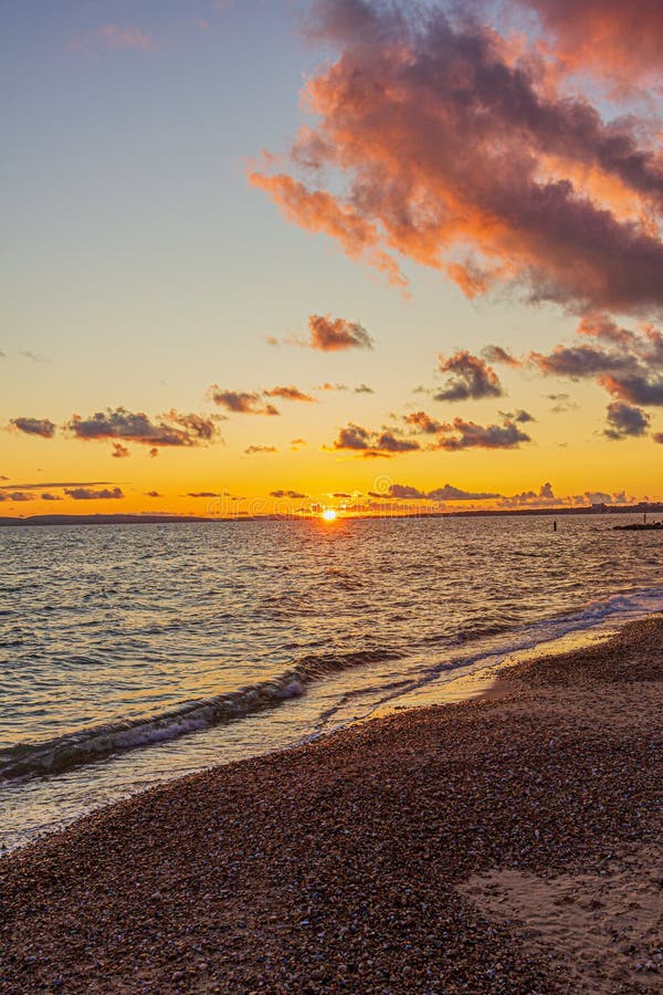 Titel: En bild av en stonstrand vid solnedgången med krasande vågor och eko under en stor gul grumlig himmel royaltyfria bilder