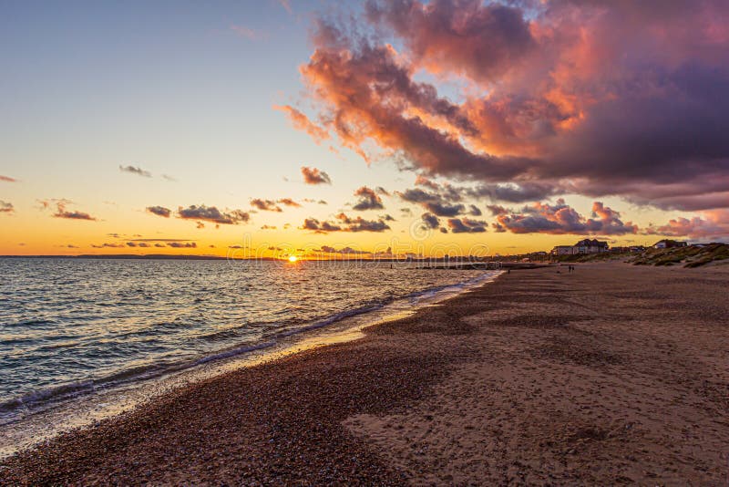 Titel: En bild av en stonstrand vid solnedgången med krasande vågor och eko under en stor gul grumlig himmel arkivfoto