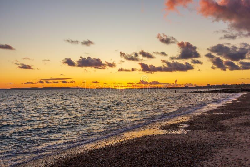 Titel: En bild av en stonstrand vid solnedgången med krasande vågor och eko under en stor gul grumlig himmel royaltyfri bild