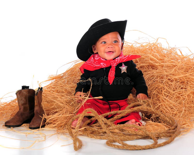 A happy biracial baby dressed as a cowboy sitting in a pile of hay. Isolated on white. A happy biracial baby dressed as a cowboy sitting in a pile of hay. Isolated on white.