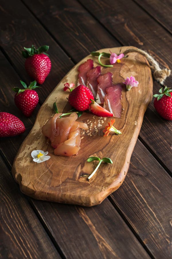 Tnąca deska z prosciutto, bekonem i truskawkami na drewnianym tle, Mi?sna p??misek zak?ska obraz royalty free Tnąca deska z prosciutto, bekonem i truskawkami na drewnianym tle, Mi?sna p??misek zak?ska obraz royalty free