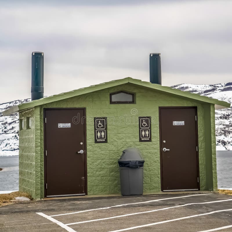 Toalete público unisex do quadro quadrado contra a montanha nevado do lago e o céu nebuloso no inverno fotos de stock Toalete público unisex do quadro quadrado contra a montanha nevado do lago e o céu nebuloso no inverno fotos de stock