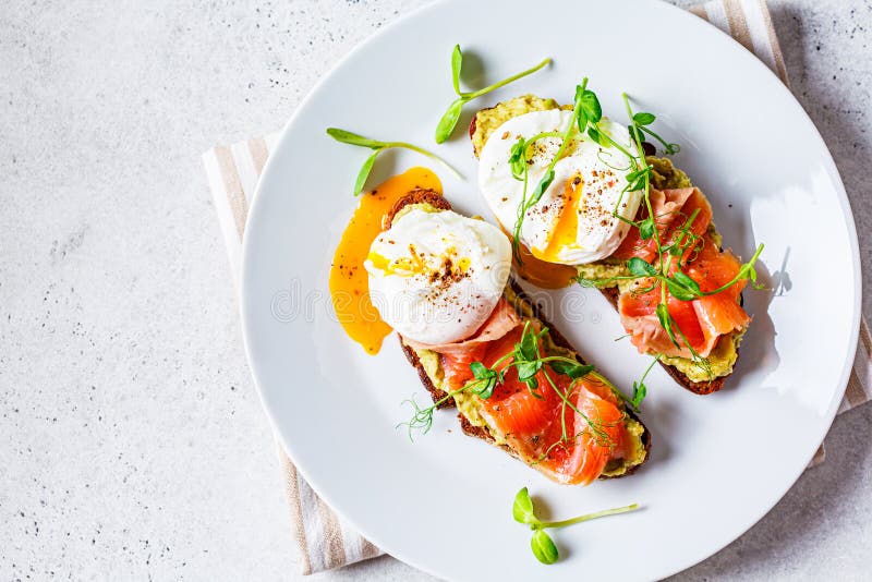 Toast with salmon, poached egg and avocado on white plate, top view. Poached egg with salmon and guacamole on rye bread